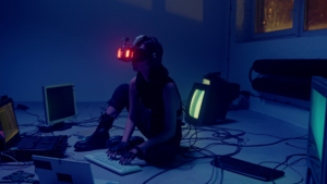 A female hacker sitting on the floor having its right leg wrapped and typing on a computer keyboard surrounded by multiple electronic devices and cables wearing a VR goggles headset utilizing VISION.